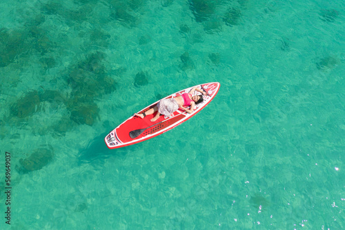 Aerial top view of Asian woman, a tourist, paddling a boat, canoe, kayak or surfboard with clear blue turquoise seawater, Andaman sea in Phuket island in summer season, Thailand. Water in ocean © tampatra