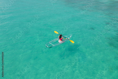 Aerial top view of Asian woman, a tourist, paddling a boat, canoe, kayak or surfboard with clear blue turquoise seawater, Andaman sea in Phuket island in summer season, Thailand. Water in ocean