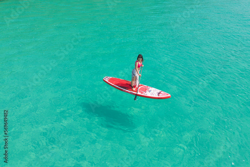 Aerial top view of Asian woman, a tourist, paddling a boat, canoe, kayak or surfboard with clear blue turquoise seawater, Andaman sea in Phuket island in summer season, Thailand. Water in ocean © tampatra