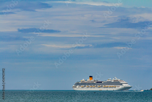 navio de cruzeiro navegando em águas calmas no horizonte e uma pequena lancha passando ao seu lado em dia de sol, céu azul e algumas nuvens. photo