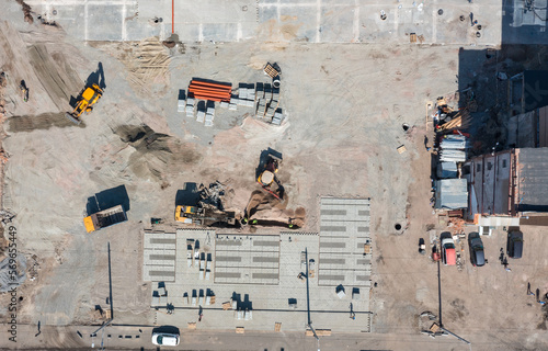 drone photo of a construction site. Excavator digs a hole, workers in helmets. On the ground building material