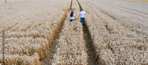 a couple in love in white t-shirts and jeans walks through a field of wheat holding hands. Harvester marks on the field