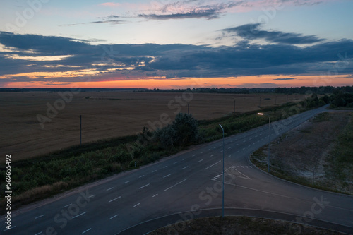 crossroads at sunset. Lanterns are lit against the sunset sky. The road goes between the fields. The sky is still orange. Dramatic drone photo.