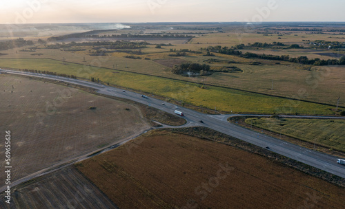 the highway curves in a turn on a U-turn. The track goes between the fields against the backdrop of the sunset sky. Cars are driving along the road. Drone photo