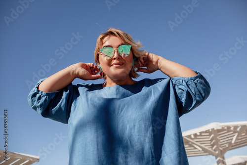 Beautiful woman plus size is walking against the background of nature in the sea. The adult woman is wearing a black maxi stylish dress. A woman of large size holds the cup pf coffee