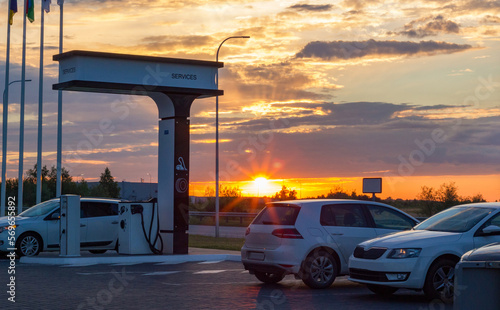 cars are parked at the gas station. Two in the parking lot, one white - in the service area. Orange sky on the horizon