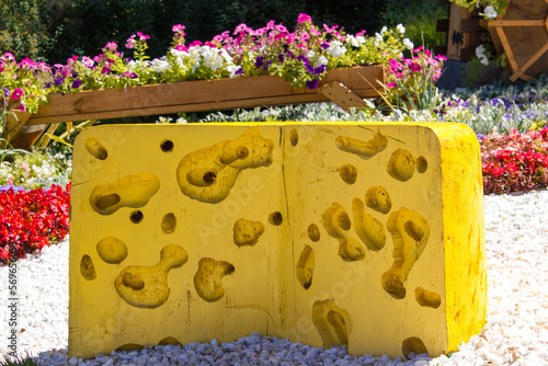 a mock-up of a piece of yellow cheese with holes lies against the background of a flower bed. landscape design