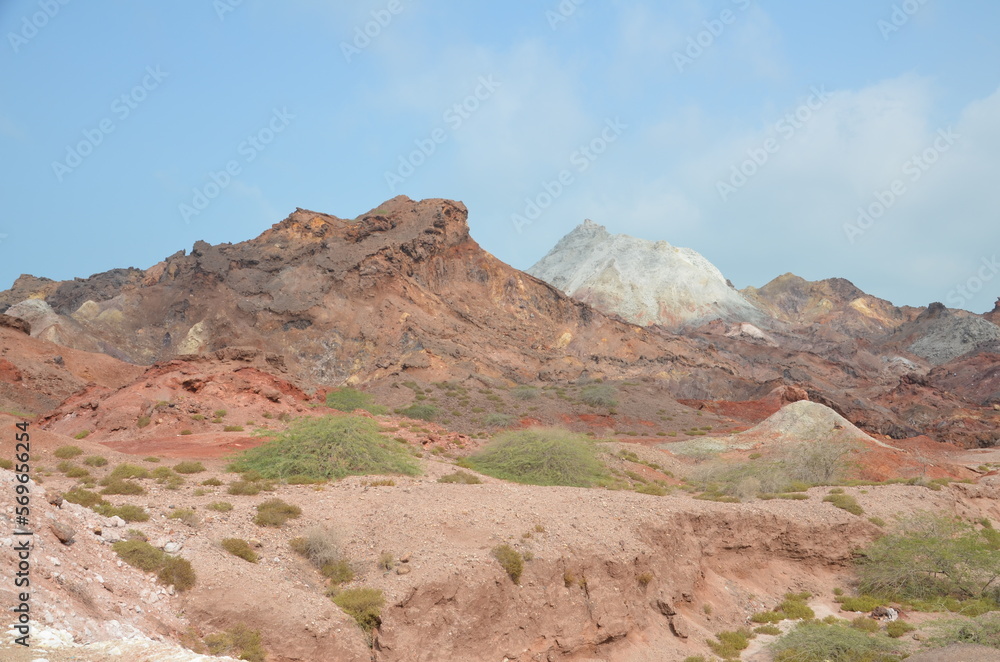 barren landscape with some low plants and beautiful colored mountains in background at Hormuz island, Iran