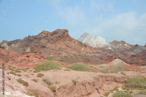 barren landscape with some low plants and beautiful colored mountains in background at Hormuz island, Iran © Holger