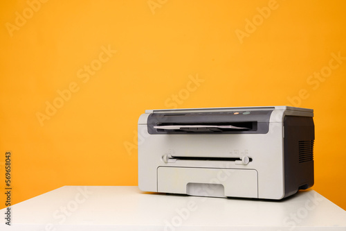 Front view of a light printer and a blank A4 paper on a white table on a yellow background, mockup.Office equipment, close-up.Copy space.Multifunction device. Multifunction printer.