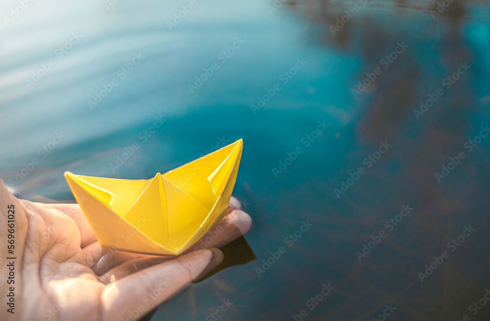 Yellow lonely floating paper boat in hand. Colorful sailing ship in big blue spring puddle, river water.Warm wet rainy weather.Hello spring,autumn.Children play,have street fun outdoors.Way to future