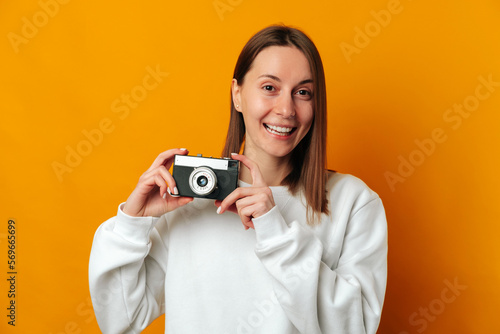 I love my job as a photographer says a young smiling woman holding a camera over yellow background.