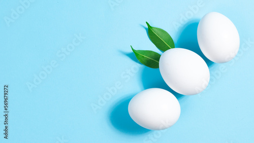 Three white chicken eggs on blue background. Natural green leaves like the ears of an Easter bunny