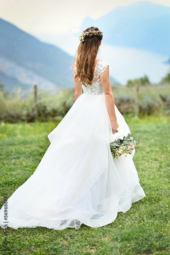 Fototapeta premium Bride in a white dress stands, holding her bouquet behind her back