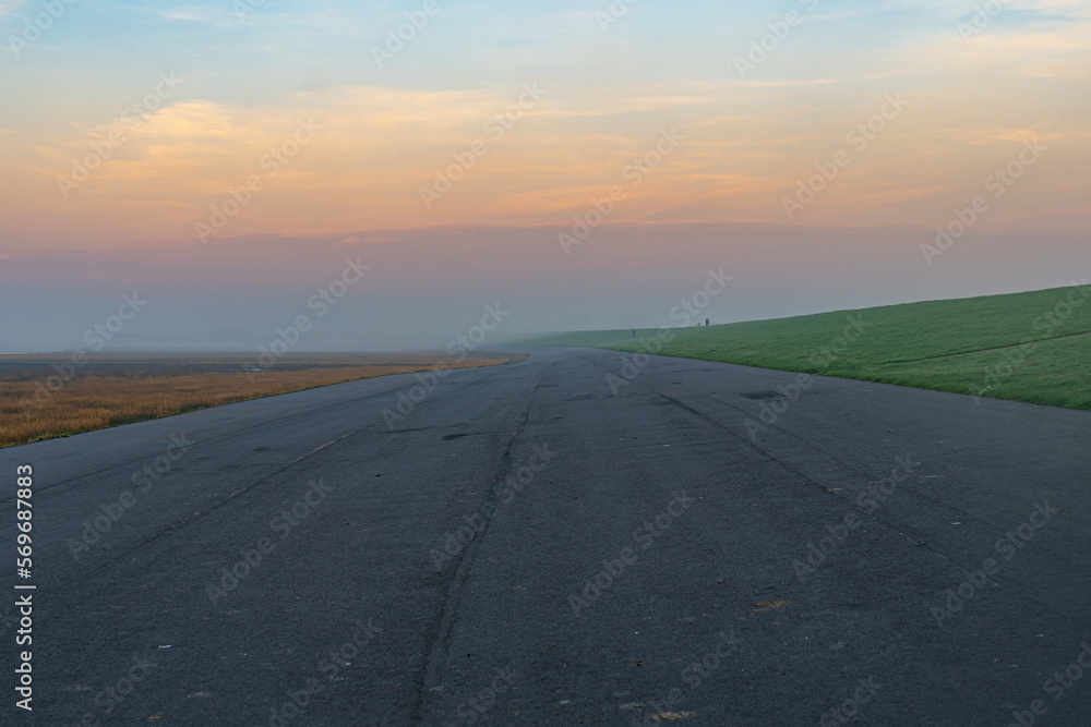 Fototapeta premium Dike of the seaside resort Norddeich in the northwest of East Frisia directly on the North Sea coast. Ground fog and the play of colors of the sunset invite you to take a walk by the sea