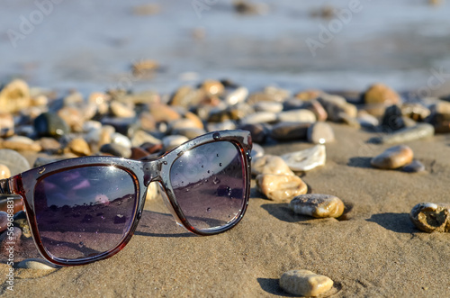 Sunglasses lie on a sandy and rocky seashore against the backdrop of sea waves