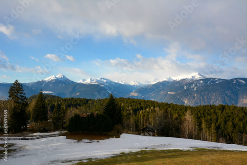 There is a tourist cottage under the snowy mountains near the forest. Forested winter mountain massif