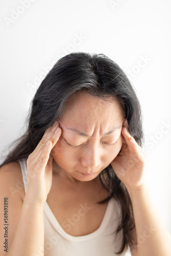 Young Asian girl wearing casual white T-shirt over isolated background suffering from headache desperate and stressed because pain and migraine. Hands on head. © Mykola