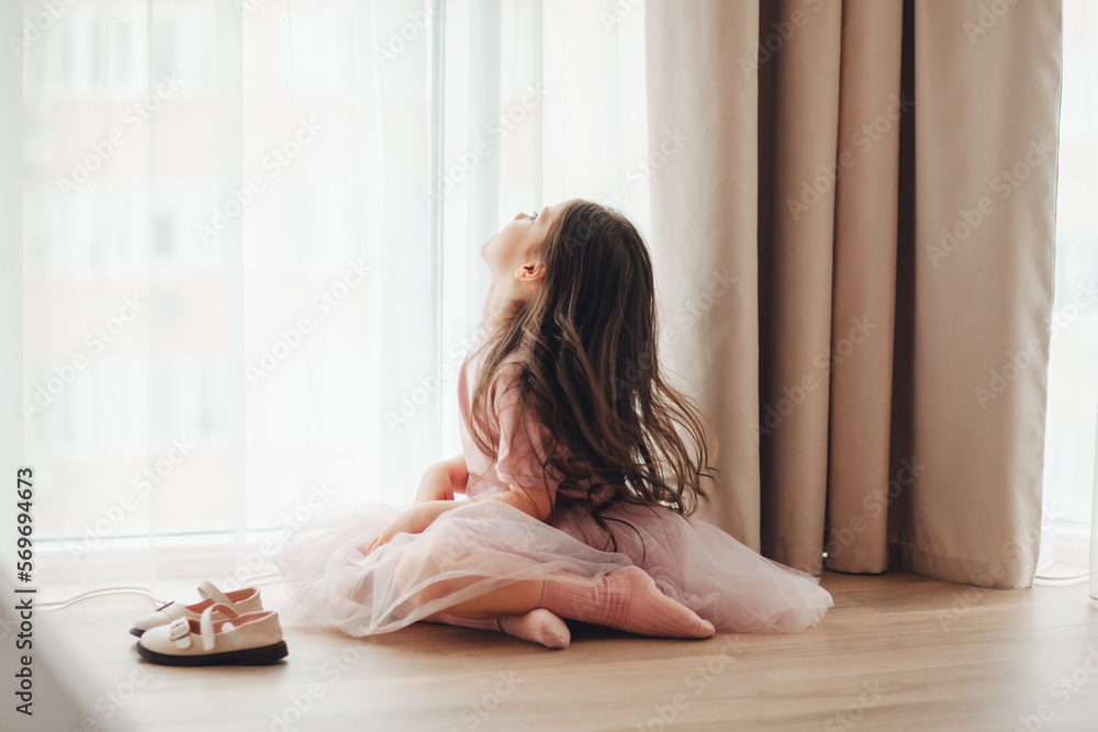the little girl took off her shoes and sat down to rest near the window on the warm floor. cozy and comfortable house. the little girl took off her shoes and sat down to rest near the window on the warm floor. cozy and comfortable house.