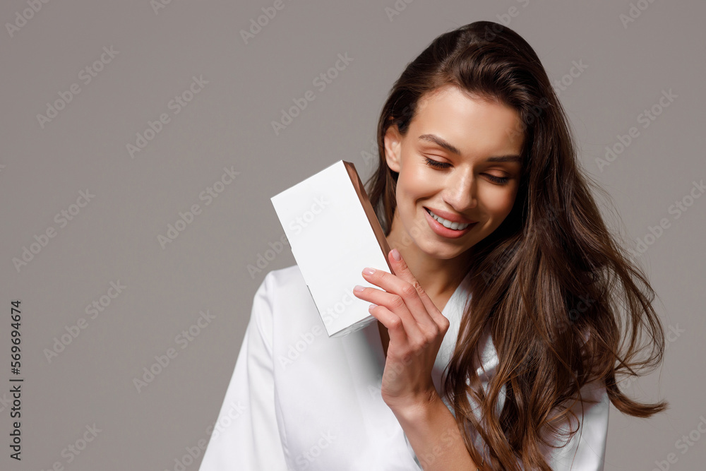 Φωτογραφία A beautiful young cosmetologist doctor in a white medical suit smiles at the camera and holds cosmetology products in her hands