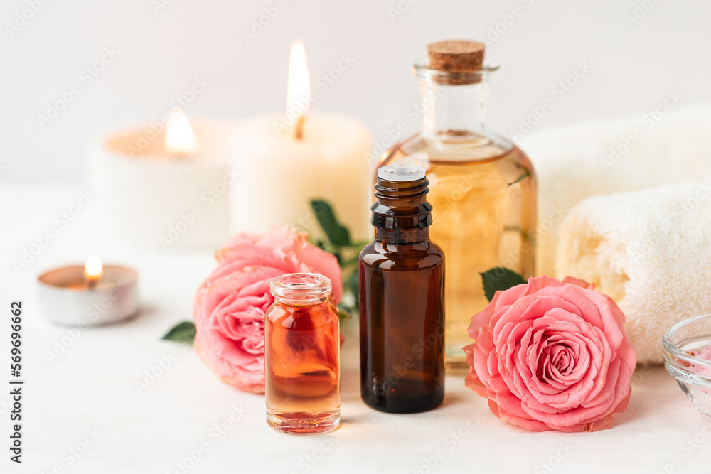 Aromatherapy. Concept of pure organic essential rose oil. Elixir with plant based floral or herbal ingredients. Pink flowers extract. Spa atmosphere with candle, towel. White background Aromatherapy. Concept of pure organic essential rose oil. Elixir with plant based floral or herbal ingredients. Pink flowers extract. Spa atmosphere with candle, towel. White background