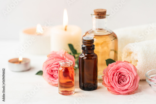 Aromatherapy. Concept of pure organic essential rose oil. Elixir with plant based floral or herbal ingredients. Pink flowers extract. Spa atmosphere with candle  towel. White background