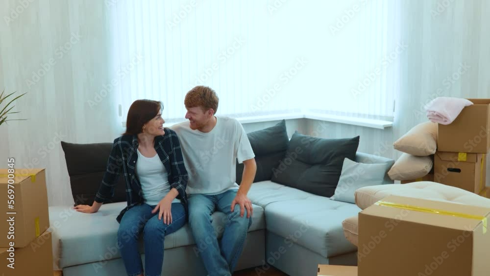 Camera moving back from happy couple sitting on sofa in new apartment with many boxes. Relocation concept. Moving day. Marriage relations. Husband surprised his beloved wife Real time Camera moving back from happy couple sitting on sofa in new apartment with many boxes. Relocation concept. Moving day. Marriage relations. Husband surprised his beloved wife Real time