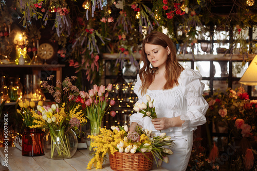A young beautiful woman florist takes care of flowers in a cozy flower shop and collects bouquets. Performs an online order for flowers at a local store. Small business.