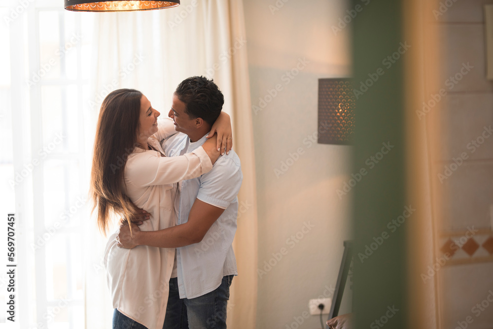 Fototapeta premium Beautiful young couple at home. Hugging, kissing and enjoying spending time together while celebrating new flat apartment. Real estate mortgage black man and caucasian woman. House owner celebration