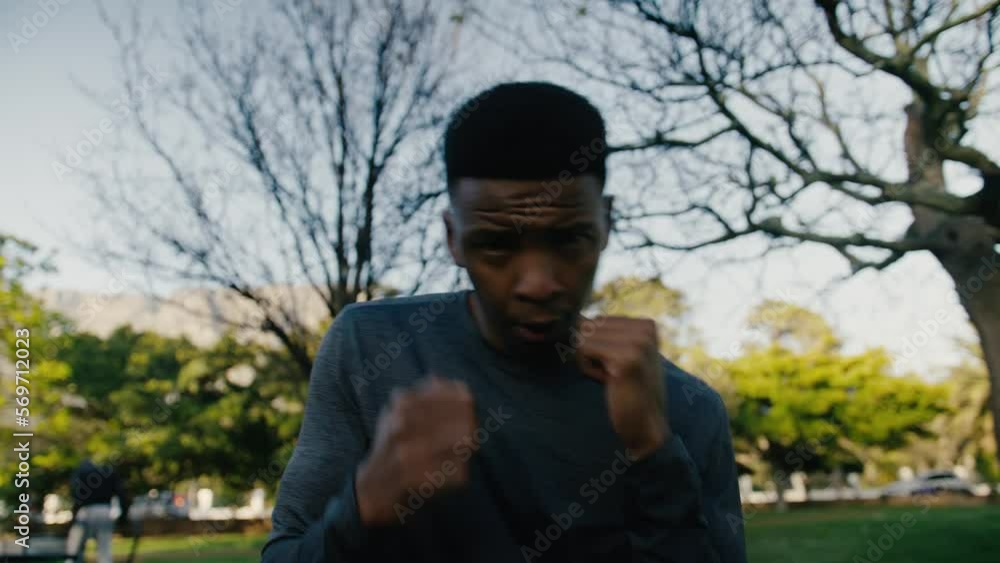 Young black man in sweatshirt punching the air during boxing training in park Young black man in sweatshirt punching the air during boxing training in park