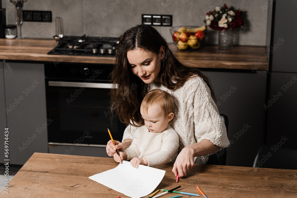 Mom and toddler daughter draw pictures with colored pencils and spend time with mother together. Developing drawing lesson for child toddler at home. Maternity leave. Mom and toddler daughter draw pictures with colored pencils and spend time with mother together. Developing drawing lesson for child toddler at home. Maternity leave.