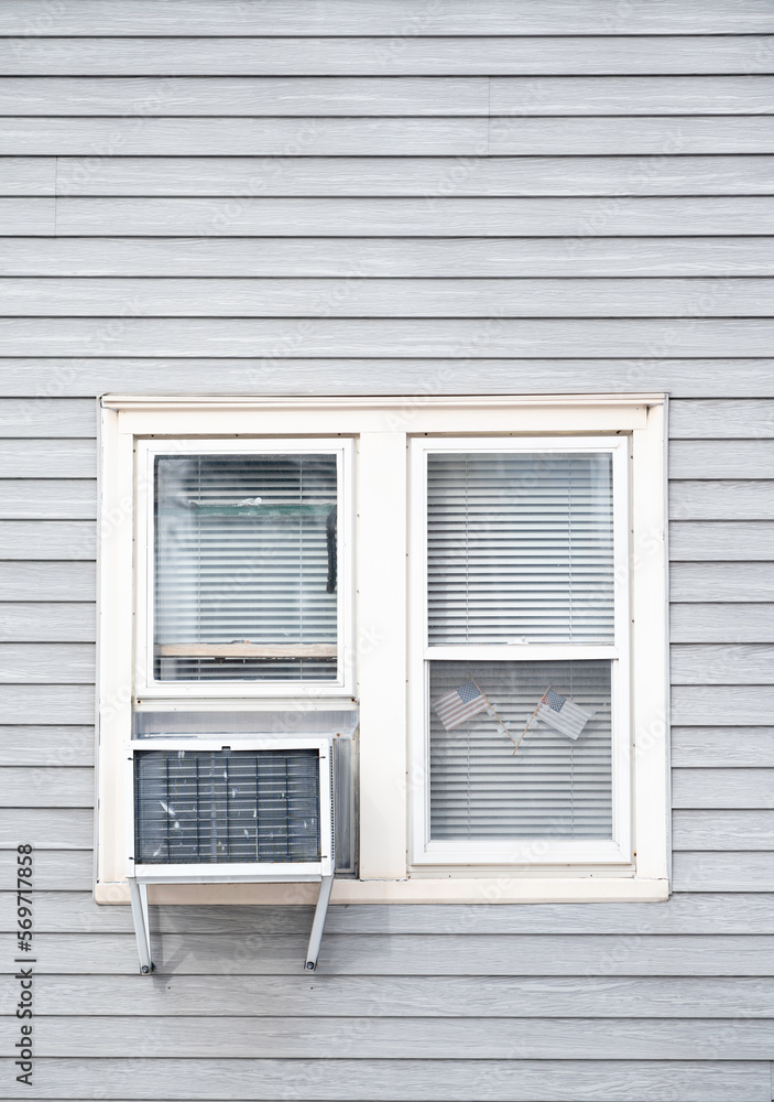 An exterior view of a pair of windows with an air conditioner and two faded American flags