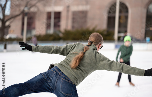 Fototapeta Naklejka Na Ścianę i Meble -  A man with a ponytail wearing blue jeans and a sweatshirt ice skates in downtown Milwaukee in the winter
