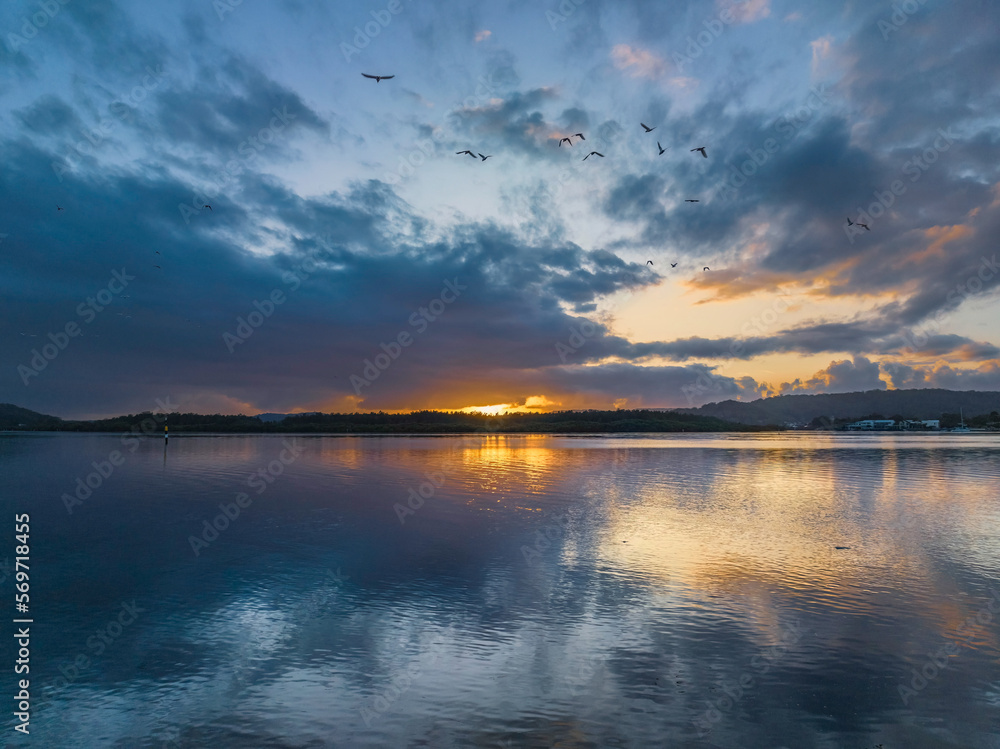 Obraz premium Sunrise waterscape with rain clouds, birds and reflections