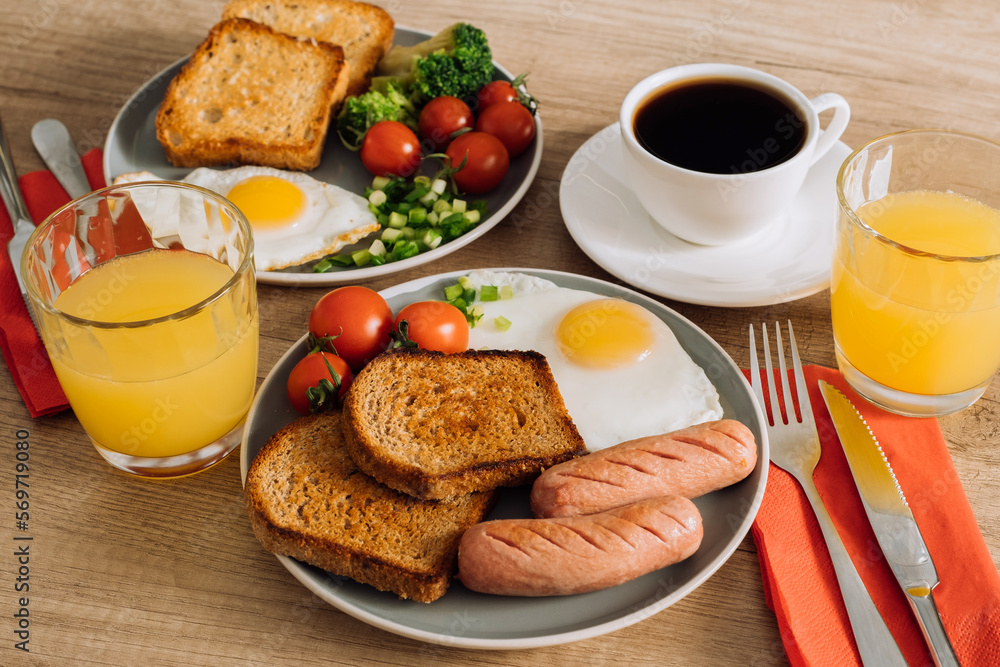 Grilled sausage and whole wheat toast with fried egg and cherry tomatoes, English breakfast with cup of black coffee and orange juice Grilled sausage and whole wheat toast with fried egg and cherry tomatoes, English breakfast with cup of black coffee and orange juice