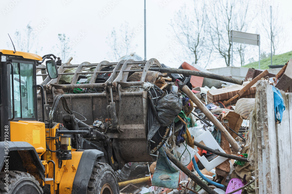 Fototapeta premium Heavy construction machine, front end loader moving along recycling center area, close up view. Waste management industry concept.