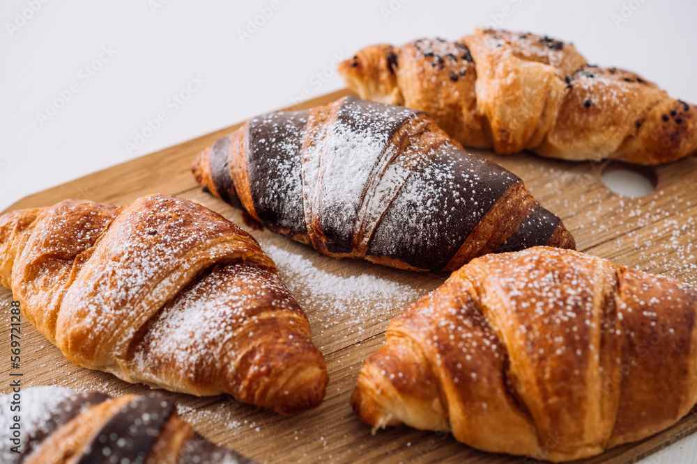 Close up bunch of appetizing brown and chocolate croissants with powdered sugar on a wooden board on white table