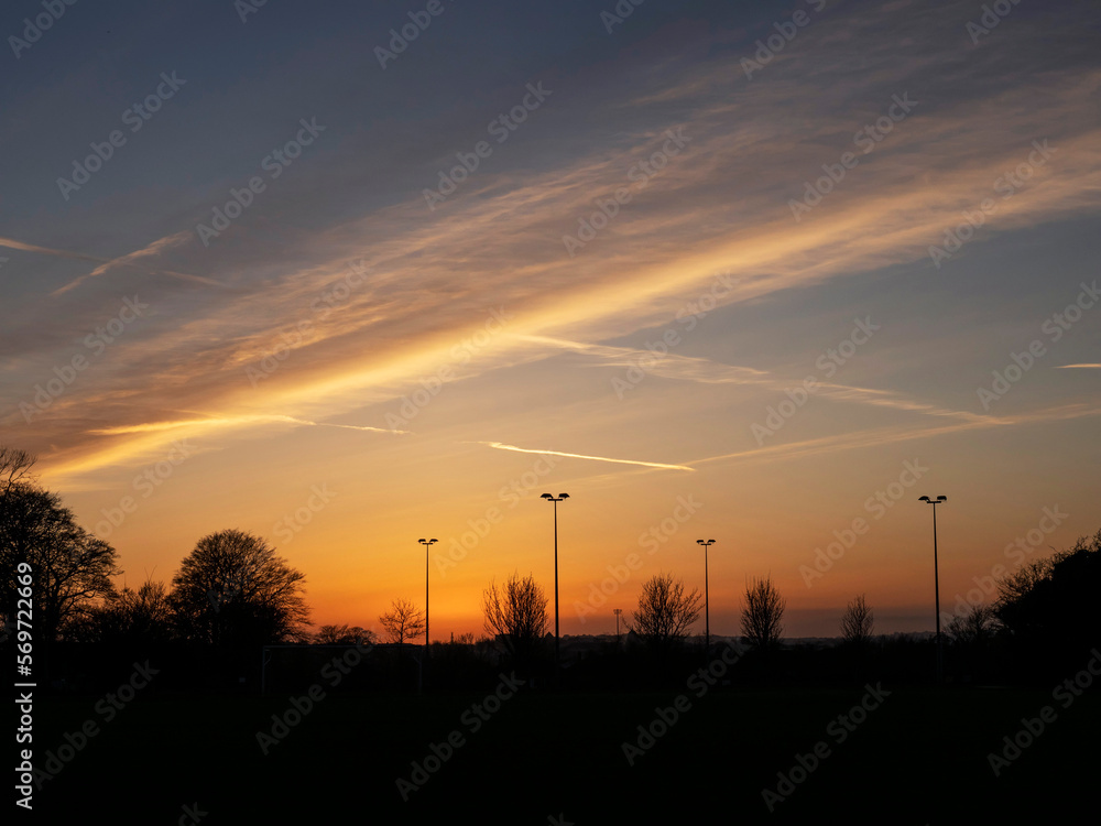 Rich sunset sky over trees silhouette. Beautiful nature scene. Nobody. Tall light poles in the background. Rich sunset sky over trees silhouette. Beautiful nature scene. Nobody. Tall light poles in the background.