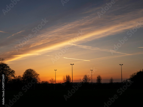 Rich sunset sky over trees silhouette. Beautiful nature scene. Nobody. Tall light poles in the background.