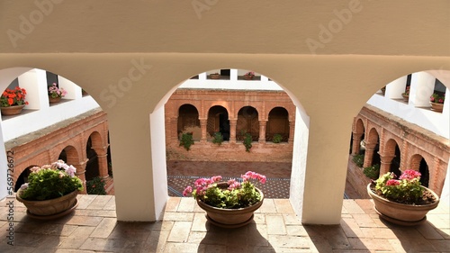  View through the white arches of the upper level of the Mudejar cloister at La Rábida Franciscan Friary decorated by colorful geraniums in winter sun, Palos de la Frontera, Spain photo