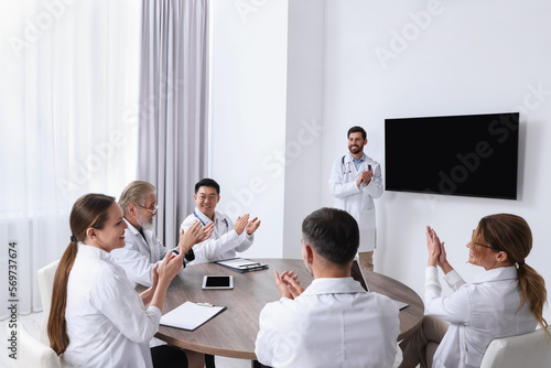 Team of doctors listening to speaker report near tv screen in meeting room. Medical conference