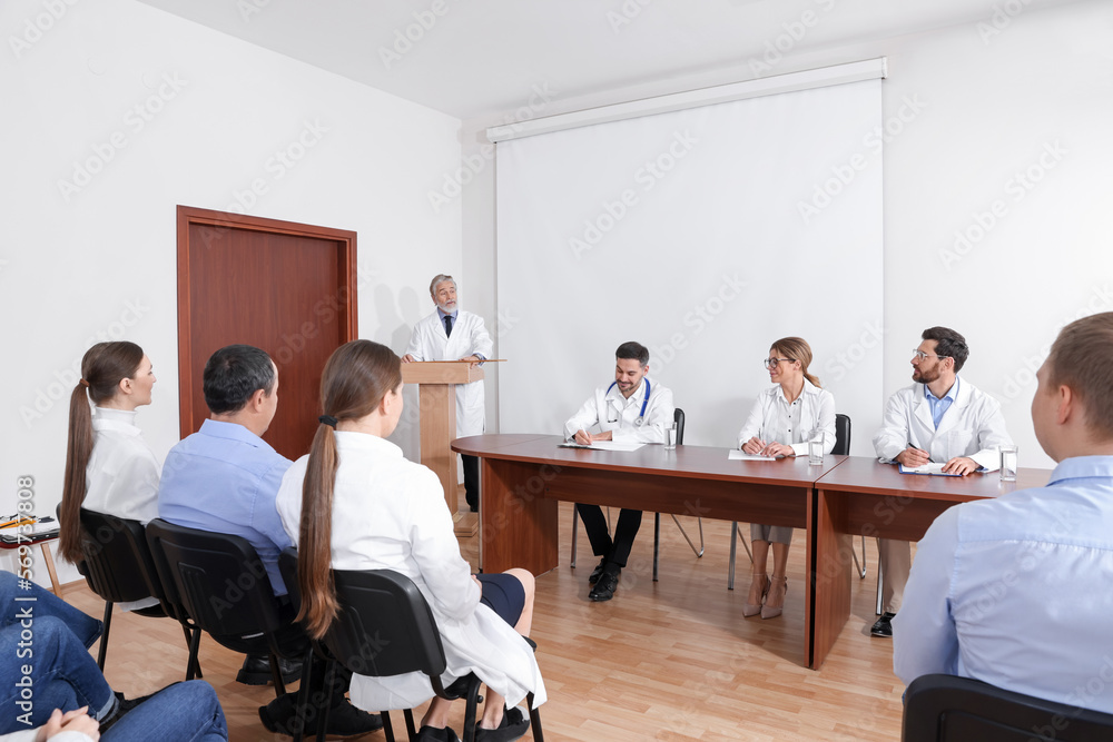 Senior doctor giving lecture in conference room with projection screen