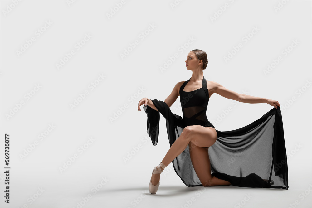 Graceful young ballerina practicing dance moves with black veil on white background. Space for text