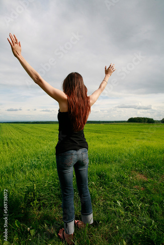 Rear view of woman looking out over farmland with arms raised high.