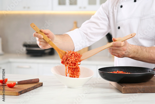 Professional chef putting delicious spaghetti into bowl at marble table in kitchen, closeup