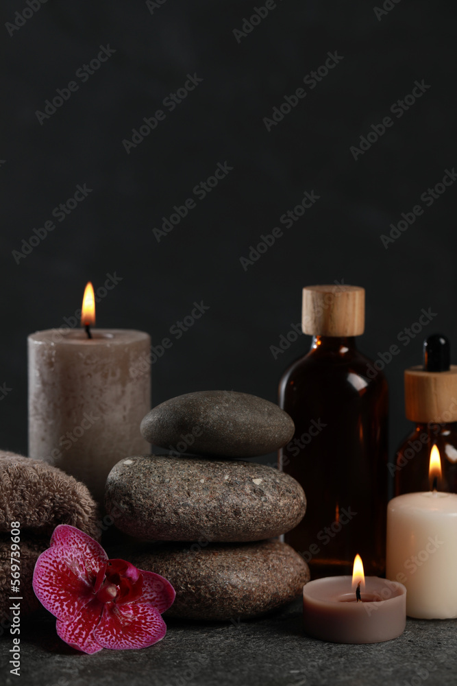 Beautiful composition with burning candles, spa stones and different care products on dark grey table