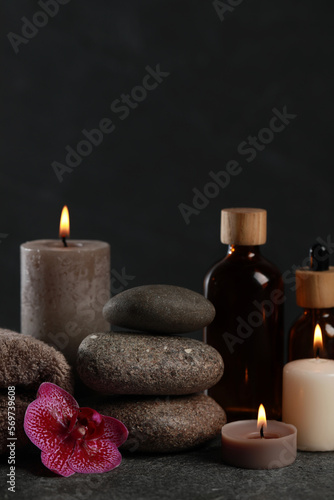Beautiful composition with burning candles, spa stones and different care products on dark grey table