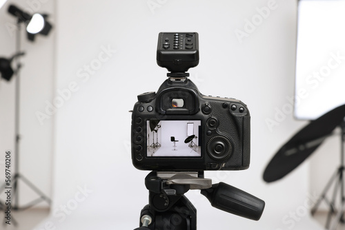 Tripod with camera, bar stool and professional lighting equipment in modern photo studio, focus on screen
