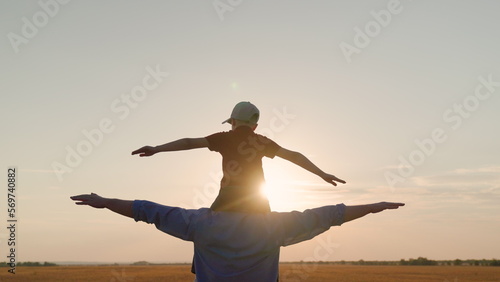 Father Son play together in front of sun, dream, fly. Dad, child fantasize, kid aviator sits on his fathers shoulders. Concept of happy family, childhood dream. Boy plays pilot airplane, hands wings