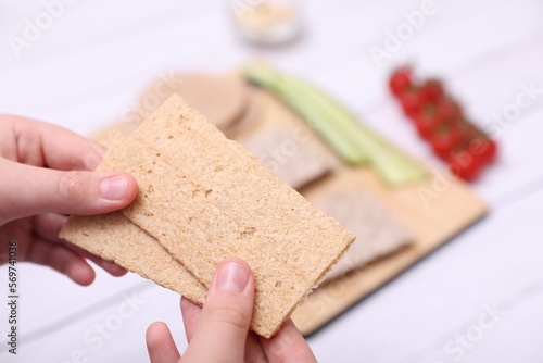 Woman holding tasty crispbreads at white wooden table, closeup photo